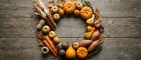 Autumn harvest wreath with pumpkins, apples, corn, nuts and fall leaves arranged in circle on rustic wooden background for seasonal decoration and thanksgiving.