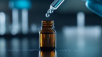 Liquid drops falling from glass dropper into amber medicine bottle against blurred blue laboratory background, dramatic lighting highlights essential oil.