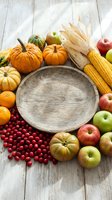 Autumn harvest arrangement with empty wooden bowl surrounded by pumpkins, apples, corn, and cranberries on whitewashed wood surface for seasonal and thanksgiving designs.
