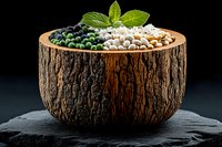 Assorted legumes in rustic wooden bowl with fresh mint garnish on black slate background, showcasing natural food ingredients for healthy cooking.