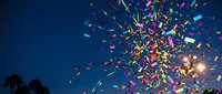 Colorful confetti explosion against deep blue twilight sky with palm trees silhouettes creating festive celebration atmosphere for party events.