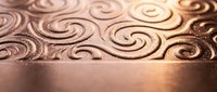 Elegant copper metal surface with intricate swirl patterns and warm golden lighting creating luxurious decorative background for premium design projects.