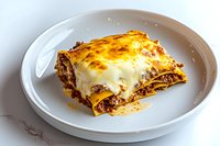 Traditional layered lasagna with ground beef, melted mozzarella and bechamel sauce on white ceramic plate, close up view of homemade Italian pasta dish.