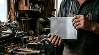 Craftsman holding blank metal sheet in workshop with tools and equipment, showcasing metalworking, fabrication, and industrial craftsmanship for design mockups.