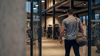Athletic Caucasian man walking into modern fitness gym carrying sports bag, ready for workout session in contemporary training facility.