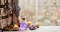 Dried lavender bundles with essential oil bottle, amethyst crystals and candles create peaceful spa atmosphere for aromatherapy and wellness rituals.