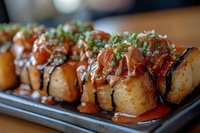 Takoyaki balls topped with spicy sauce, green onions and bonito flakes served on dark plate. Traditional Japanese street food close up with selective focus.