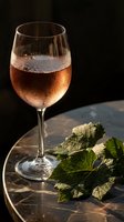 Elegant rose wine glass with condensation droplets on dark wooden surface with grape leaves for sophisticated dining and celebration moments.