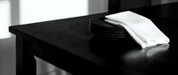 Black table with stacked plates and folded napkin in monochrome minimalist interior design setting for home decor and lifestyle projects.
