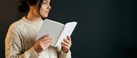 Young woman in cozy cream sweater reading book with peaceful expression against dark background for relaxation and leisure lifestyle concepts.
