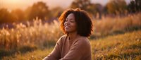 Young African American woman with curly hair enjoying peaceful moment in golden sunset field, eyes closed in meditation and gratitude outdoors.