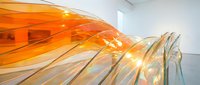 Flowing orange and amber glass ribbons with translucent layers creating dynamic movement and light refraction in modern interior space. Contemporary art installation.