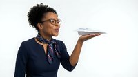 Professional African American flight attendant in navy uniform holding serving tray with smile, isolated on white background for aviation industry designs.