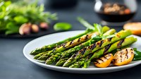 Grilled green asparagus spears and roasted lemon slices served on white plate against dark background, fresh seasonal vegetables for healthy eating.