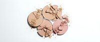 Broken rose gold makeup powder compacts scattered with crushed cosmetic powder on white background for beauty and fashion design projects.