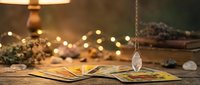 Mystical tarot cards spread on wooden table with crystal pendulum and warm fairy lights creating atmospheric fortune telling scene for spiritual guidance.