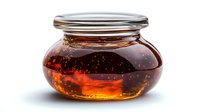 Organic honey in round glass jar with metal lid on white background, golden amber liquid with bubbles showing natural crystallization pattern.
