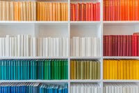Colorful books arranged by spectrum colors on white bookshelf, creating rainbow pattern. Modern minimalist library organization shows gradient from blue to red.
