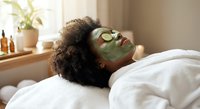 Young African American woman relaxing with green clay face mask and cucumber slices on eyes during spa treatment at home wellness routine.