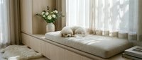Cozy reading nook with built-in bench seating, soft cushions and white flowers by sunny window. Minimalist interior design for relaxation and comfort.