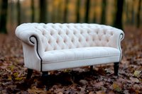 Elegant white tufted chesterfield sofa outdoors in autumn forest setting with fallen leaves, showcasing luxury furniture photography and interior design.