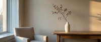Minimalist living room interior with natural sunlight streaming through window, featuring beige armchair, wooden table and ceramic vase with dried branches.