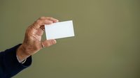 Senior man with tanned skin holding blank white business card against olive green background, suitable for corporate branding and professional marketing materials.