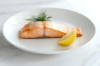 Grilled salmon fillet with fresh dill and lemon wedge served on white plate against marble background, minimalist food presentation for restaurant menu.