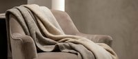 Cozy beige throw blanket draped over comfortable armchair in modern living room interior creating warm atmosphere for home decor and relaxation.
