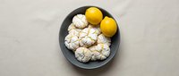 Fresh cauliflower florets and bright yellow lemons arranged on dark ceramic plate against neutral beige background for healthy cooking and nutrition.