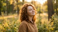 Young redhead woman with curly hair enjoying peaceful moment in autumn park during golden hour sunset with warm natural lighting and blurred background.