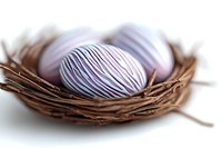 Delicate purple and white striped Easter eggs nestled in rustic twig nest against soft white background, creating serene seasonal composition for holiday designs.