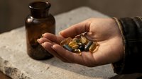 Male hand holding golden supplement capsules with amber glass bottle on stone surface for wellness and health.