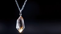 Crystal pendant with amber-tinted point hanging from silver chain against dark background, showcasing natural mineral jewelry for spiritual or fashion accessories.