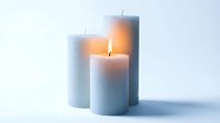 Three soft gray pillar candles with a warm glowing flame on a light background, creating a calm and cozy atmosphere for home decor concepts.
