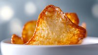 Crispy golden potato chips with delicate texture on white plate against blurred bokeh background, macro food photography highlighting crunch and detail.