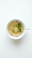 Overhead view of herbal tea with chamomile and rose petals in white porcelain cup on light background, suitable for wellness and beverage content.