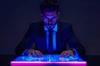 Young Hispanic businessman in suit working on futuristic glowing touchscreen interface in dark room illuminated by neon blue and purple light, creating dramatic cyberpunk atmosphere.