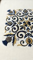 Elegant floral embroidery with navy blue and gold thread on white fabric featuring ornate swirls, flowers and decorative elements for luxury textile design.