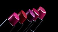 Vibrant pink and red lipsticks arranged in diagonal line on black background showcase glitter and matte finishes, creating dramatic cosmetic composition.