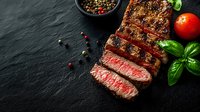Juicy grilled beef steak sliced on black stone background with fresh basil, cherry tomato and mixed peppercorns, medium rare doneness with pink center.