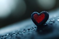 Heart-shaped pendant with red center and dark border covered in water droplets on wet surface creating romantic mood for love concepts.