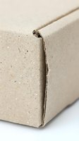 Damaged cardboard box corner showing wear and tear from shipping or storage with visible cracks and frayed edges on beige packaging material.