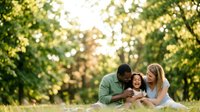 Man and woman with young child lying on grass in park, enjoying outdoor family time together.