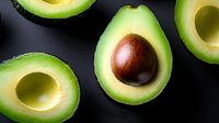 Fresh ripe avocado halves with pit on black background, close up view. Raw organic food concept for healthy eating and nutrition.