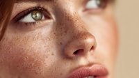 Close-up portrait of young Caucasian woman with natural freckles and green eyes in soft sunlight for beauty and skincare concepts.