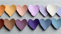 Colorful paper hearts arranged in rows showing gradient rainbow spectrum from warm to cool tones on textured background for craft projects.