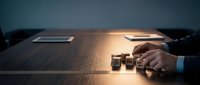 Businessman hand rolling wooden dice on conference table during strategic business meeting with documents and laptop in corporate office environment.