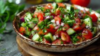 Fresh Mediterranean salad with diced tomatoes, cucumbers, red onions, and chopped herbs in rustic ceramic bowl on wooden board, vibrant healthy appetizer.