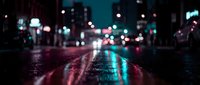 Wet asphalt street at night with colorful bokeh lights reflecting on pavement surface creating atmospheric urban scene for backgrounds and design projects.